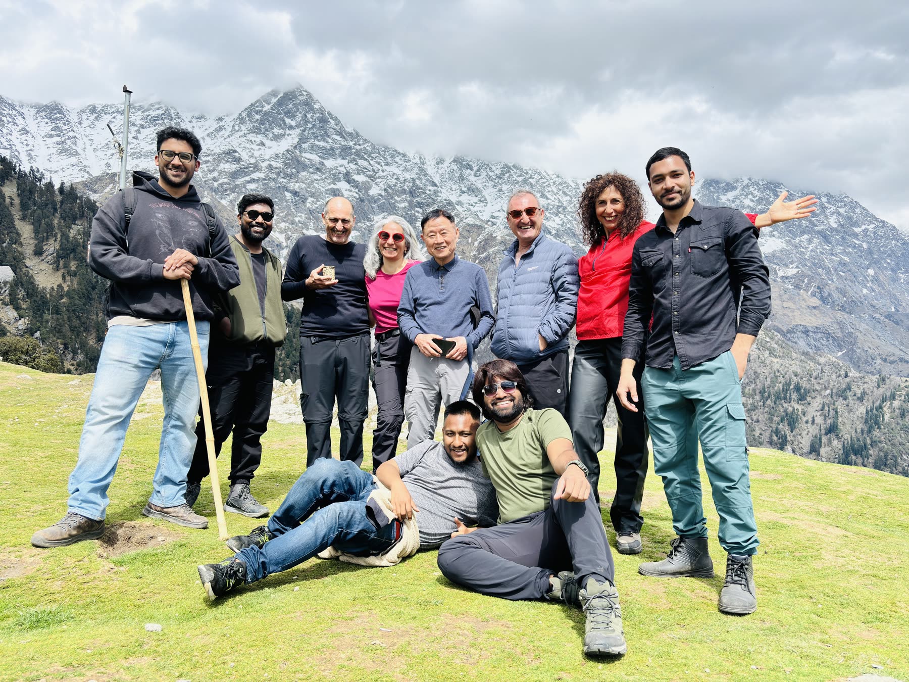 Saurav and a group of friends smiling together on a grassy ridge, with snow mountains behind